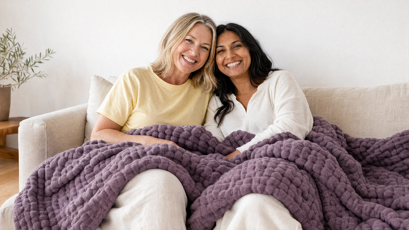Two friends relaxing on a bed under a muslin cotton blanket