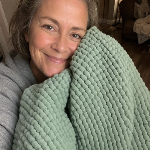 Customer photo: woman holding the Muslin Blanket in Green up beside her face
