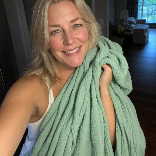 Customer photo: woman holding the Muslin Blanket in Green up beside her face