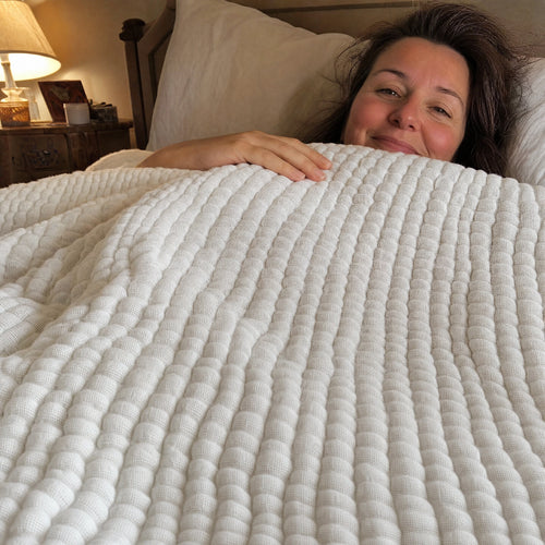 Customer photo: woman in bed tucked under the Muslin Blanket in White