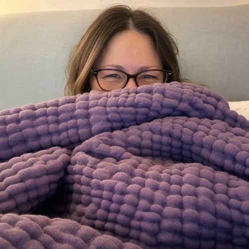 Customer photo: woman in glasses peeking over the Muslin Blanket in Purple