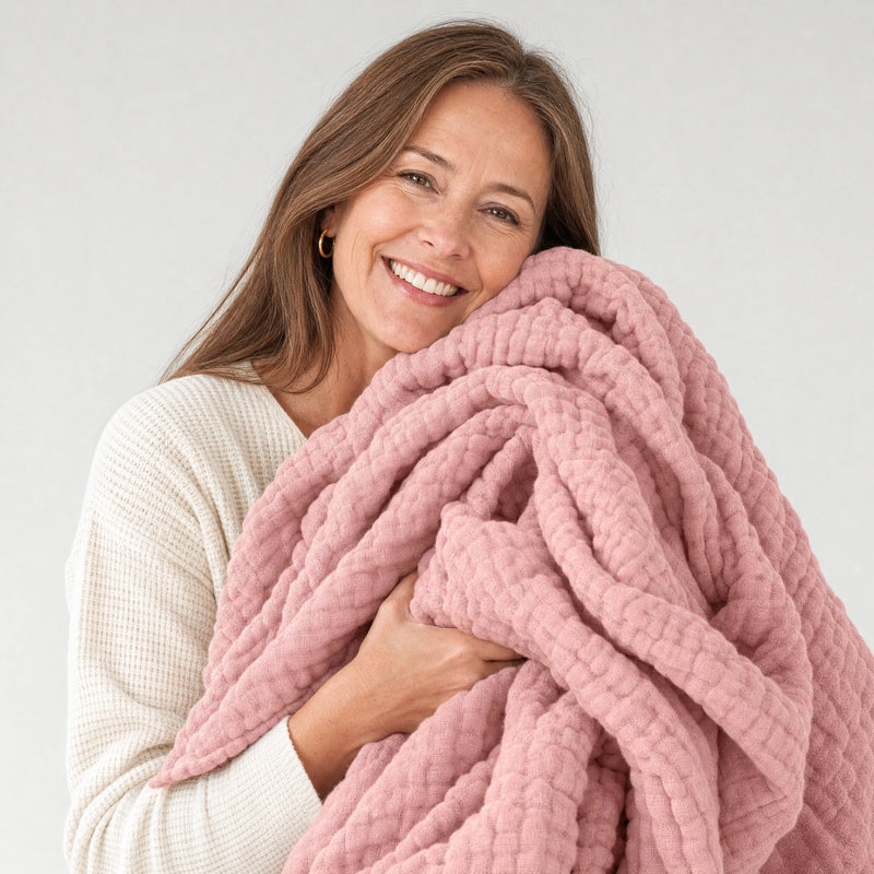 Woman holding an armful of the Muslin Blanket in Pink against her cheek