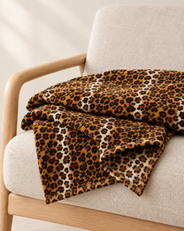 Finished bound edge of the Classic Brown leopard throw folded on an oatmeal chair