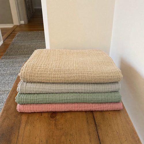 Customer photo: four folded Muslin Blankets in Dune, Grey, Green and Pink on a bed