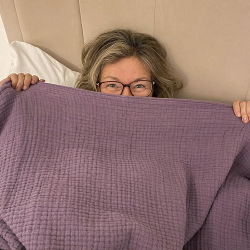 Customer photo: woman in glasses peeking over the Muslin Blanket in Purple