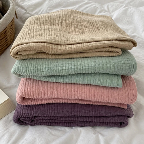 Customer photo: four folded Muslin Blankets in Dune, Green, Pink and Purple on a bed
