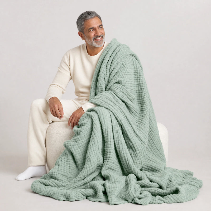 Man on a pouf with the Muslin Blanket in Green pooling on the floor