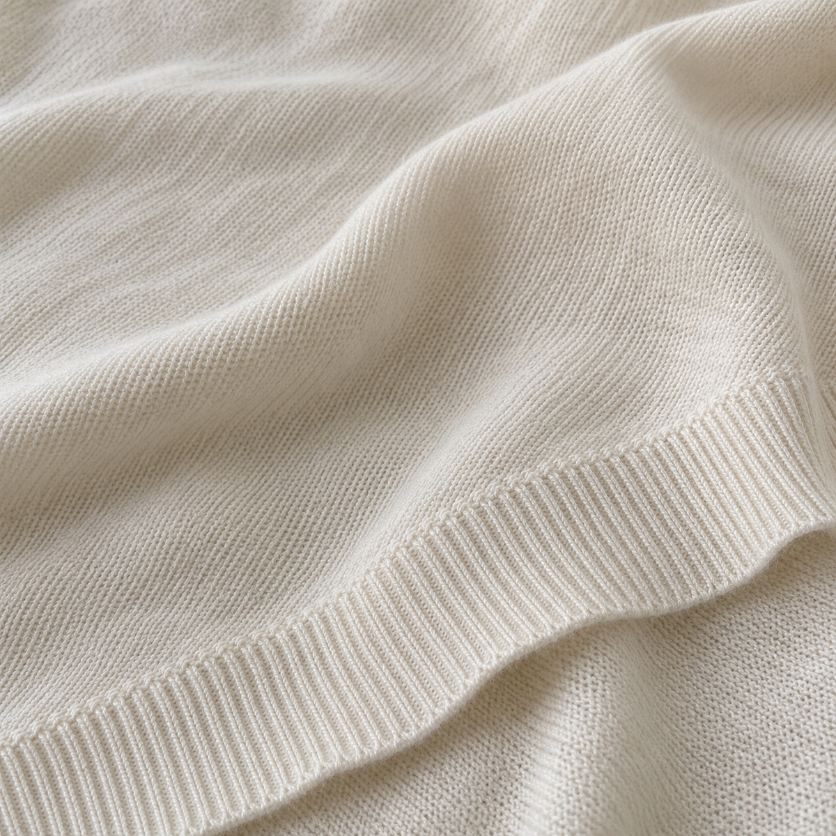 Close-up of the ivory poncho knit and ribbed hem in natural light