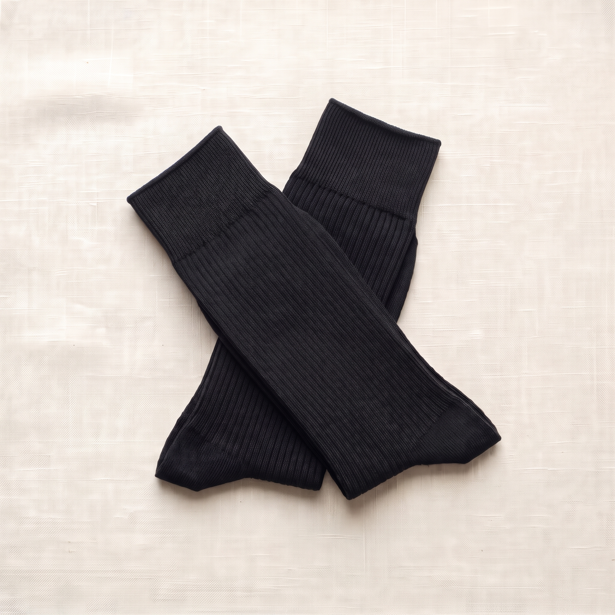 Black ribbed lounge socks folded on ivory linen; colour reference for a pack of five matching pairs.