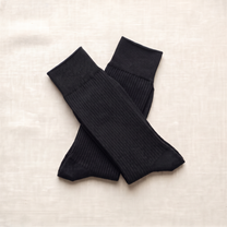 Black ribbed lounge socks folded on ivory linen; colour reference for a pack of five matching pairs.